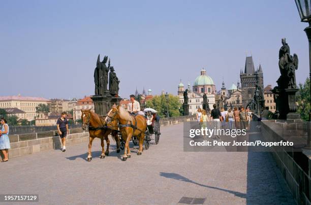 Pedestrians and a horse and carriage crossing the Charles Bridge, a medieval stone arch bridge over the Vltava River, in the city of Prague, capital...