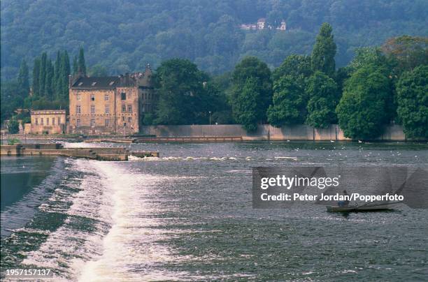 Man fishes from a rowing boat downstream from a weir on the Vltava River in the city of Prague, capital of Czechoslovakia on 19th August 1989.