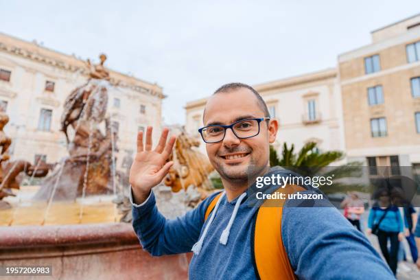 mid-adult man having a video call in front of a fountain of diana in syracuse on the italian island of ortygia - animal waving stock pictures, royalty-free photos & images