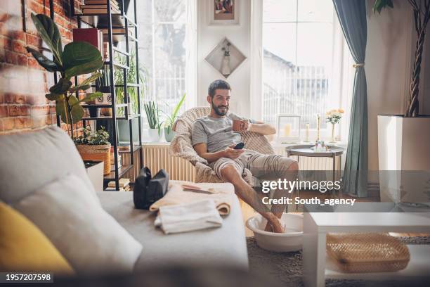 man relaxing at home having a foot bath watching tv - salon tv stock-fotos und bilder