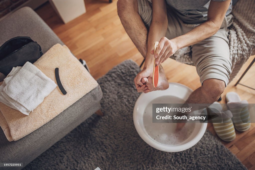 Man having foot bath at home and removing dead skin from feet