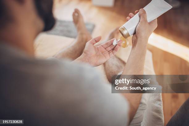 man relaxing at home and applying lotion on feet after foot bath - male feet on face stock pictures, royalty-free photos & images