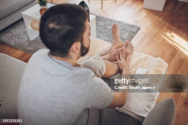 man relaxing at home and applying lotion on feet after foot bath - male feet on face stock pictures, royalty-free photos & images