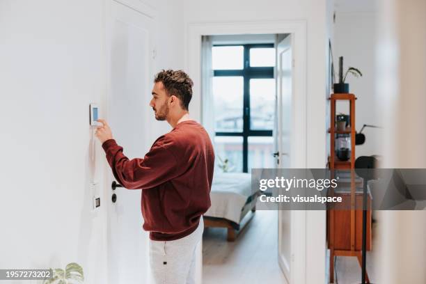 uomo che usa il termostato intelligente nella sua casa moderna - termostato foto e immagini stock