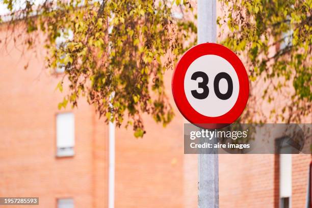 a circular traffic sign with the number thirty attached to a metal pole, branches of a tree and the wall of a building can be seen. - forbidden stock pictures, royalty-free photos & images