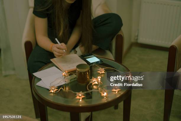 a teenage girl sitting in a chair and doing homework on her mobile phone, chatting with her friends and classmates. addiction to social networks, instant messengers and mobile applications. christmas lights, christmas eve - addiction mobile and laptop stockfoto's en -beelden