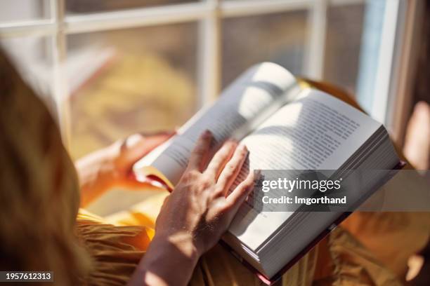 teenage girl sitting on windowsill and reading a book - lezen stockfoto's en -beelden