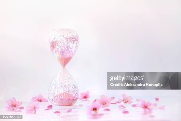 sparkling pink hourglass standing on holographic foil background with peach tree flowers spring bloom. front view, copy space. - closing time stock pictures, royalty-free photos & images