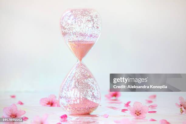 sparkling pink hourglass standing on holographic foil background with peach tree flowers spring bloom. front view, copy space. - closing time stock pictures, royalty-free photos & images