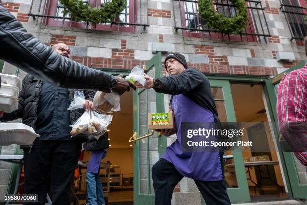 Volunteers hand out meals to a community composed of mostly newly arrived migrants at Trinity Services and Food For the Homeless, across from...