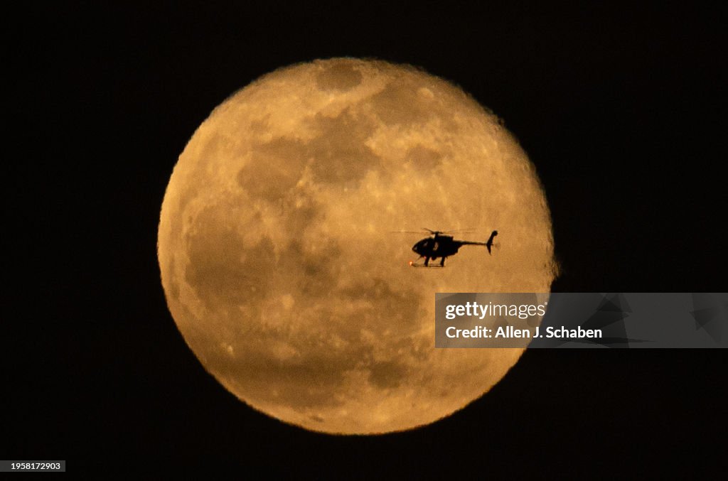 A helicopter is silhouetted by a waning gibbous moon rising as seen from Huntington Beach