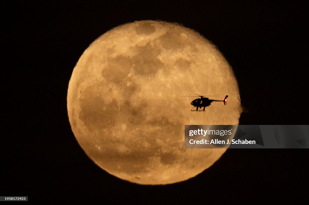 A helicopter is silhouetted by a waning gibbous moon rising as seen from Huntington Beach
