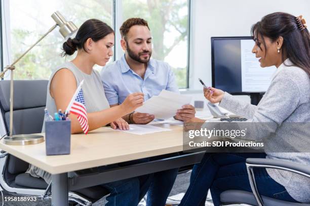 female banker explains loan paperwork to young adult couple - bank manager stock pictures, royalty-free photos & images