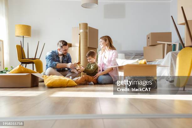 glückliche junge familie packt sachen aus kisten in neuer wohnung aus - umzug stock-fotos und bilder