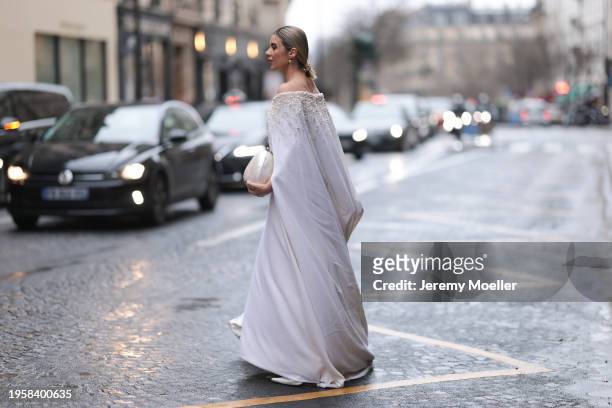 Katie Giorgadze is seen wearing a long white off-the-shoulder dress set with white pearls and a train, with pearl earrings and a mother-of-pearl bag...