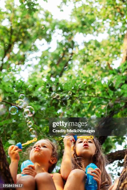 zwei mädchen blasen seifenblasen im hof - children playing in yard stock-fotos und bilder