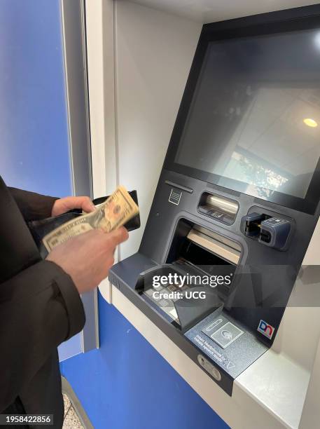 Man withdrawing money from his bank account and retrieving the cash at an ATM machine in a bank lobby. .