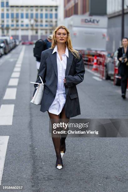 Chloe Lecareux wears black striped oversized blazer, white button shirt dress, tights, white bag outside Viktor&Rolf during the Haute Couture...