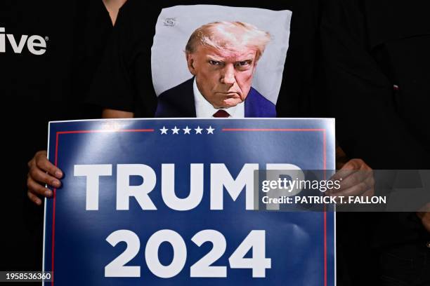 An attendee wearing the mugshot of former US President and 2024 presidential hopeful Donald Trump, holds a "Trump 2024" sign at a Commit to Caucus...