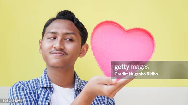 young man looking at pink heart shape balloon - indonesians celebrate valentines day stock-fotos und bilder