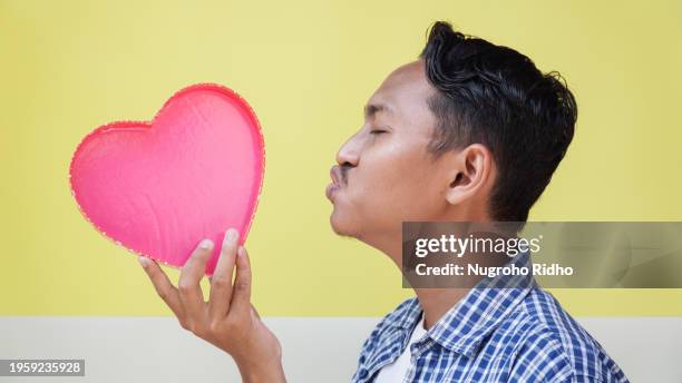 young man kiss pink heart shape balloon - indonesians celebrate valentines day stock-fotos und bilder