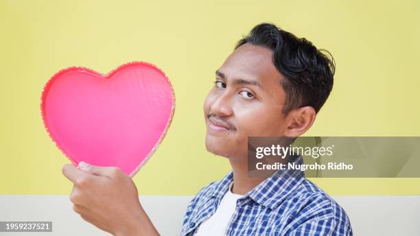 handsome man holding pink heart with loving smile - indonesians celebrate valentines day stock pictures, royalty-free photos & images