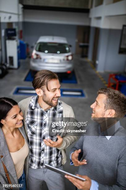 happy salesman and a couple talking while using touchpad in auto repair shop. - touchpad stockfoto's en -beelden