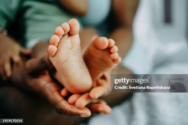 mother's hand holds black baby's leg close-up - newborn stock pictures, royalty-free photos & images