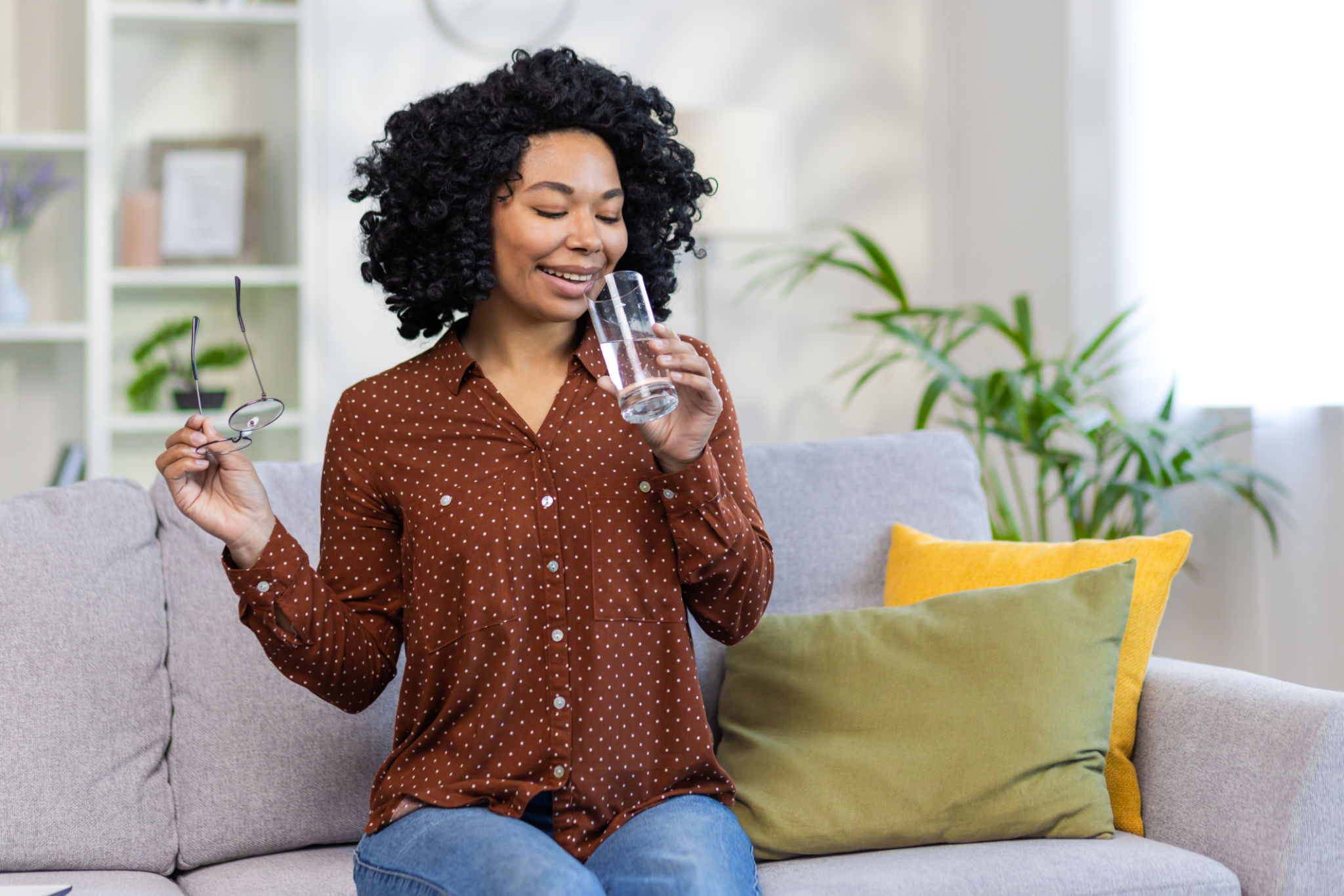 African American young woman sitting on the sofa at home and drinking clean water from a glass, quenching her thirst African American young woman sitting on the sofa at home and drinking clean water from a glass, quenching her thirst