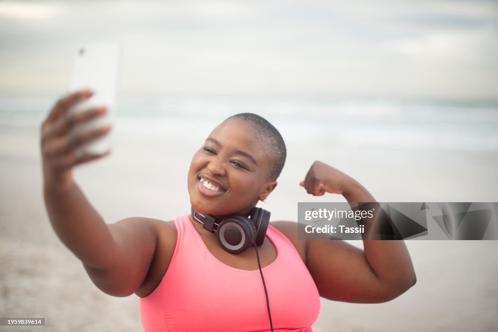 Selfie, flexing and plus size black woman at beach for health, fitness or cardio. Smile, exercise or sports and bicep muscle of happy young running athlete outdoor for strength training or workout