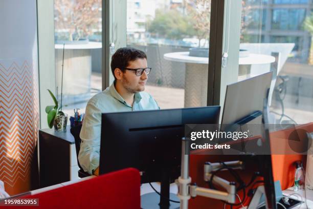 young it specialist or computer software programmer happy male looking multiple screens while working at his workplace and typing codes on a computer behind of lots of monitors - long term vision stock pictures, royalty-free photos & images