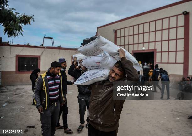 Palestinians, who left their homes and took refuge in Rafah city under hard conditions, carry the flour they received at the area where UNRWA...