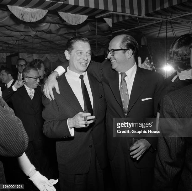 American comedian and actor Milton Berle and American comedian and actor Phil Silvers who has his right arm around Berle's shoulders, at a party,...