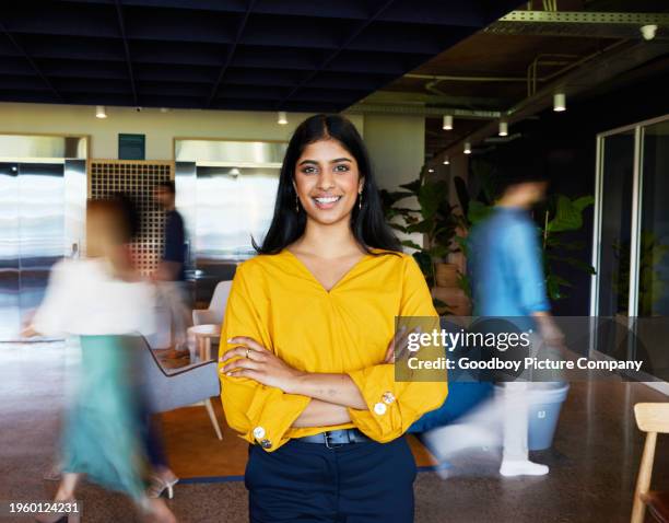 smiling businesswoman standing in an office with blurred coworkers in the background - indian corporate women background stockfoto's en -beelden