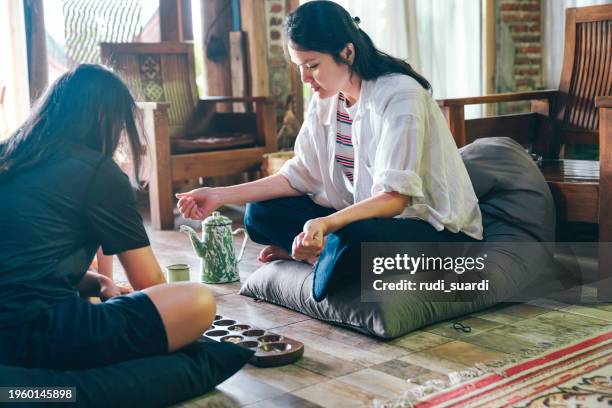 sibling  playing wari board game or congklak at home - mancala stockfoto's en -beelden