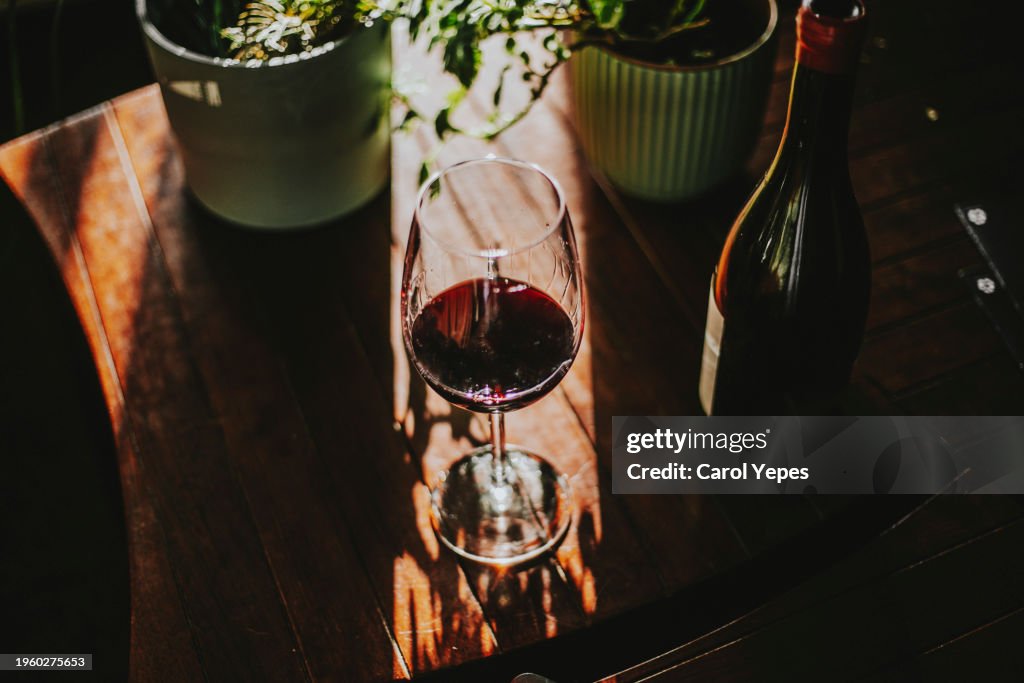 Glass of red wine sitting beside a bottle of wine, on a wooden table.