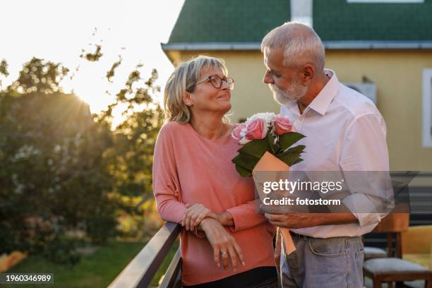 romantic man giving his loving wife flowers - wedding anniversary stock pictures, royalty-free photos & images