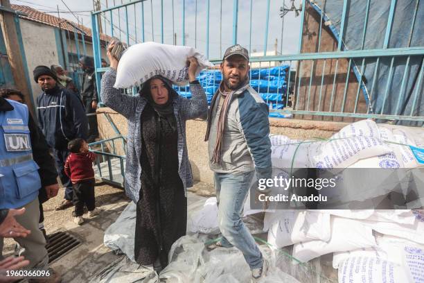 Palestinians, who left their homes and took refuge in Rafah city under hard conditions, carry the flour they received at the area where UNRWA...