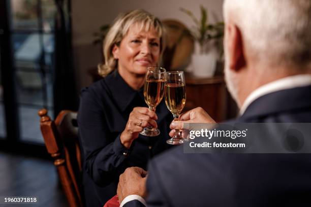 romantic couple cheering with glasses of champagne during a dinner date - wedding anniversary stock pictures, royalty-free photos & images
