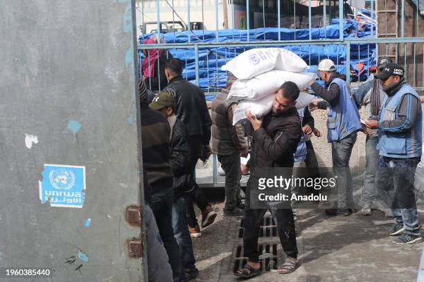 Palestinians, who left their homes and took refuge in Rafah city under hard conditions, carry the flour they received at the area where UNRWA...