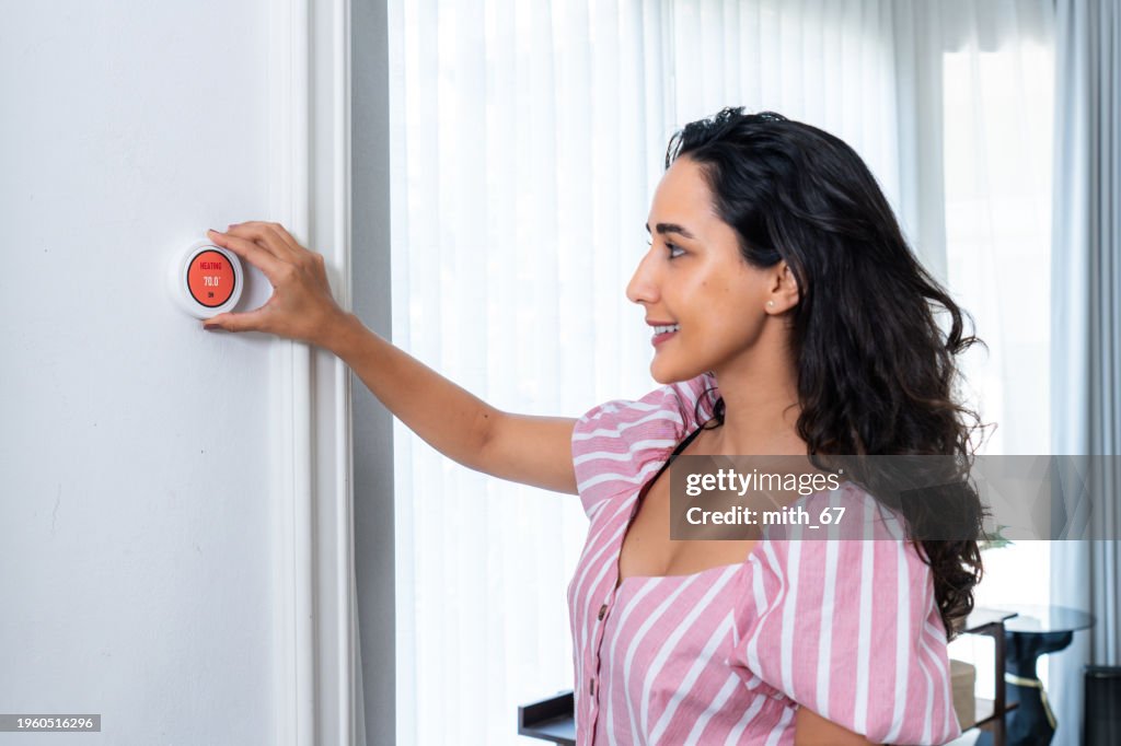 Una bella donna adulta che regola la temperatura su un termostato intelligente sul muro del soggiorno di casa durante l'inverno