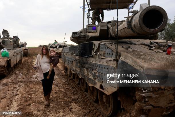 Picture taken from southern Israel from a position along the border with the Gaza Strip shows the wife of an Israeli soldier carrying her child past...