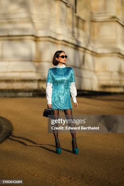 Heart Evangelista wears sunglasses, a white shirt, a blue shiny glitter fringed mini dress, a black leather crocodile mini Hermes bag, black tights,...