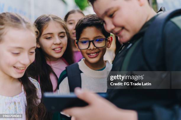 child friends watching a video on mobile phone outdoors - generation alpha stock pictures, royalty-free photos & images