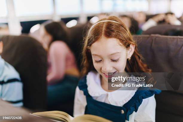 child girl reading a book on school bus - young girl reading book bus foto e immagini stock