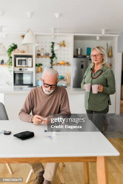 uomo anziano seduto a casa prendendo pillole di farmaci dalla bottiglia - invecchiamento della popolazione foto e immagini stock
