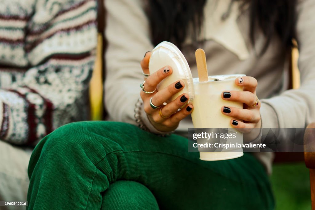 Unrecognizable woman sitting on wooden bench in park while having a smoothie