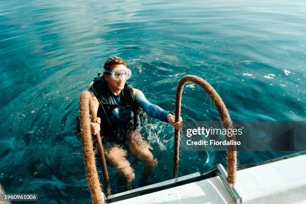 red-haired woman in diving clothes climbing the ladder from the water to the boat - high diving platform stock pictures, royalty-free photos & images