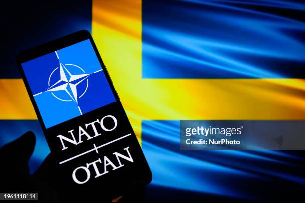 The NATO - OTAN logo is being displayed on a smart phone with the flag of Sweden in the background, in this photo illustration taken in Brussels,...