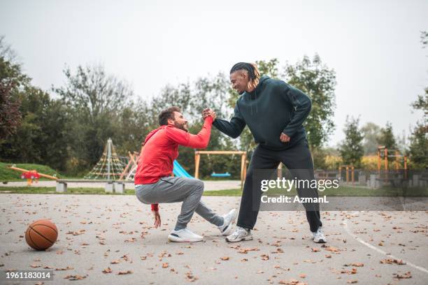schwarzer mann bietet seinem hispanischen freund auf dem basketballplatz eine helfende hand an - fairness stock-fotos und bilder